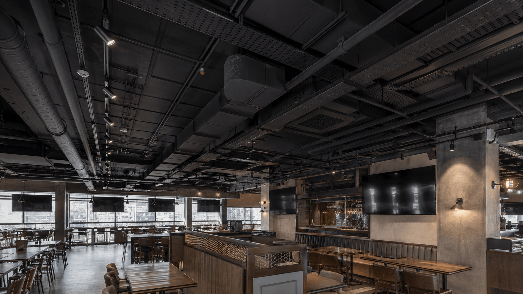 Industrial-style exposed ceiling with black-painted ducts, cable trays, and pipework left visible in a sports bar